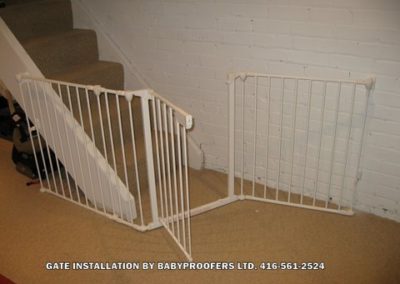 White baby gate installed at bottom of stairs where opening is slightly irregular.